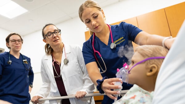 A nursing faculty member works with students in the simulation lab